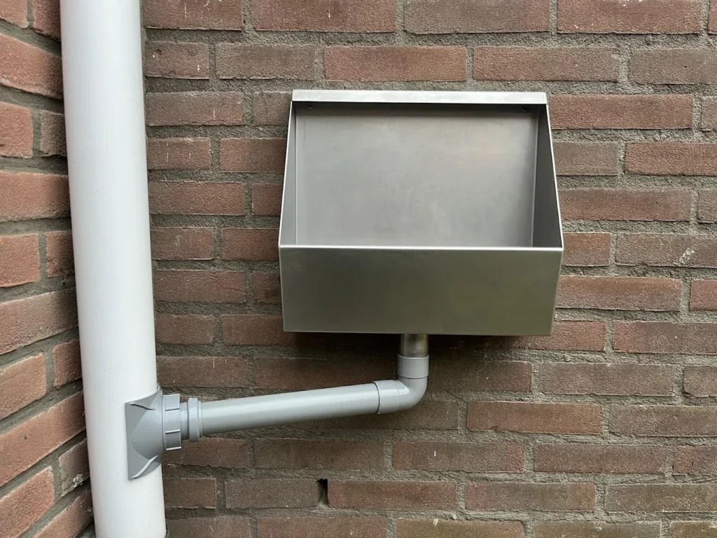 Klantfoto Jan: RVS tuinurinoir tegen bakstenen muur met grijze spoelpijp en regenpijp